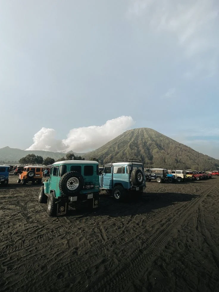 Jeep Bromo terparkir di lautan pasir dengan Gunung Bromo di kejauhan