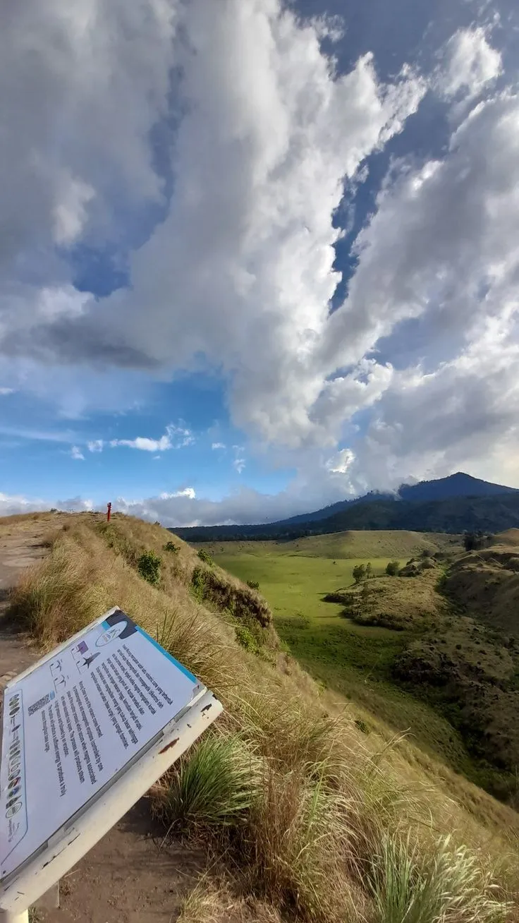 Papan informasi di lereng savana Kawah Wurung dengan langit biru berawan